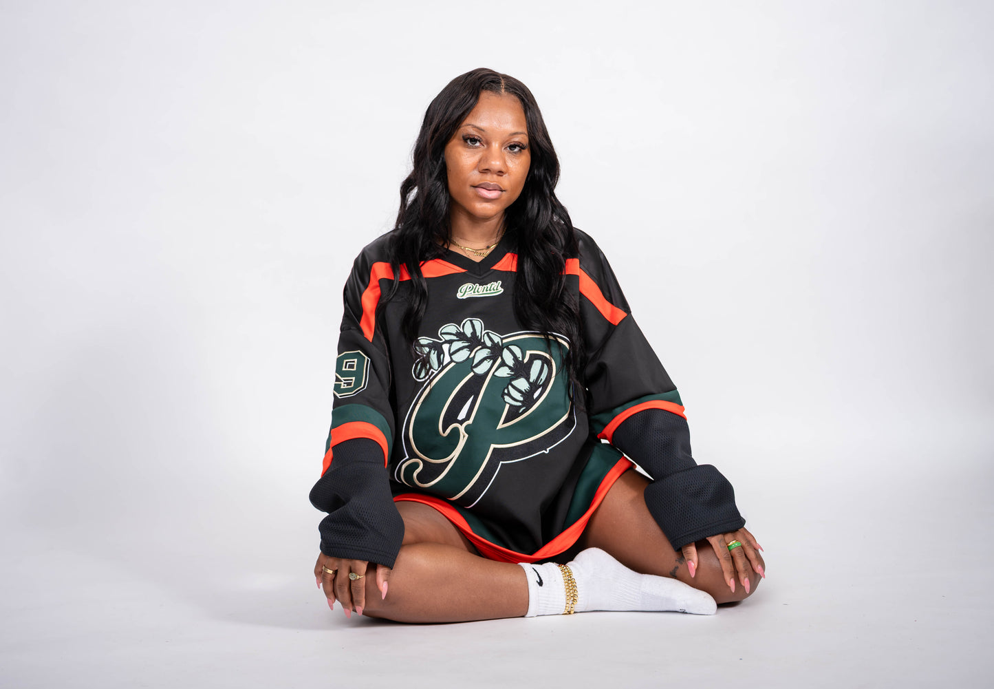 Woman wearing a black sports jersey with green and orange accents on a white background
