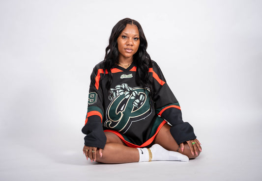 Woman wearing a black sports jersey with green and orange accents on a white background